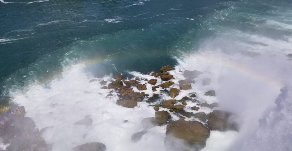 Waterfall spray from water hitting rocks with a hint of a rainbow