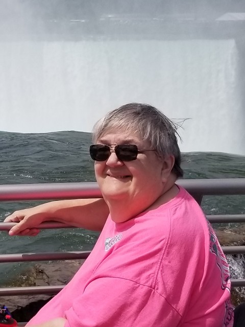 Woman in bright pink shirt with sunglasses poses in front of a waterfall